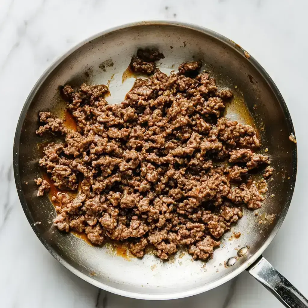 No Bean Chili Slow Cooker Recipe – Easy, Hearty & Flavor-Packed 2 ground beef browning in a stainless steel skillet on white marble for No Bean Chili slow cooker recipe