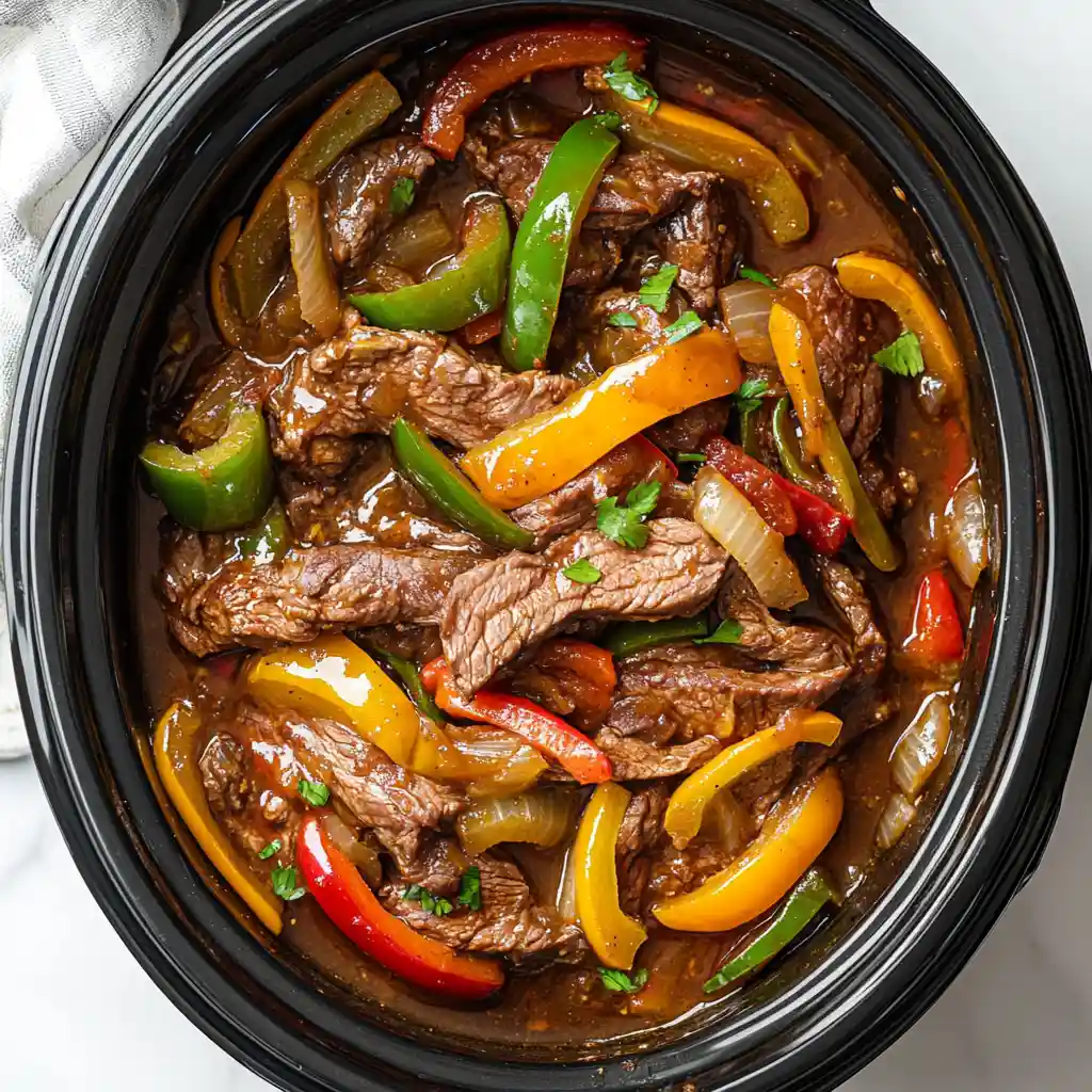 Slow Cooker Cheesesteak Quesadillas – Beef and Peppers Cooked to Perfection Cooked beef and peppers for Slow Cooker Cheesesteak Quesadillas in a black oval slow cooker